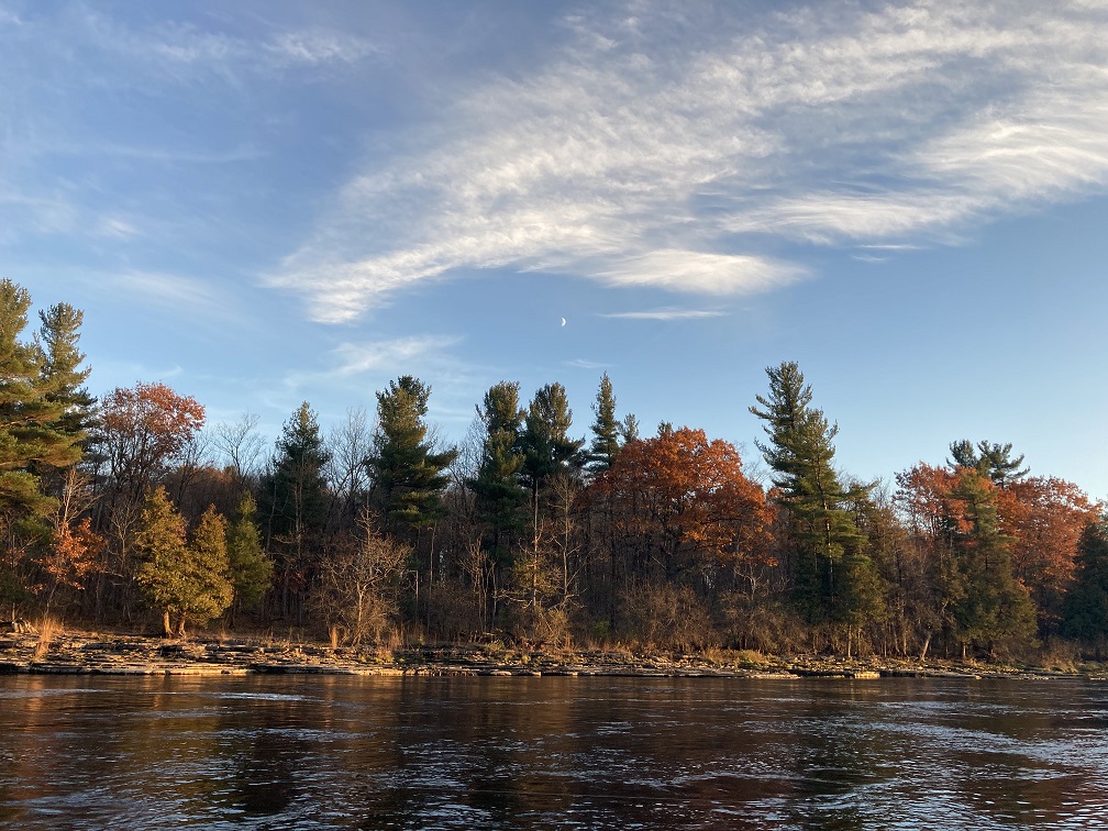Photograph of Black River New York in early fall, with a tiny sliver of the moon visible in the afternoon