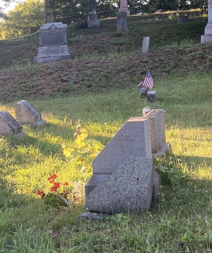 Photograph of the grave site of Cassius Coolidge, the painter.  A small bouquet of red flowers were placed in front of the gravestone and the afternoon sun is shining at the cemetery 