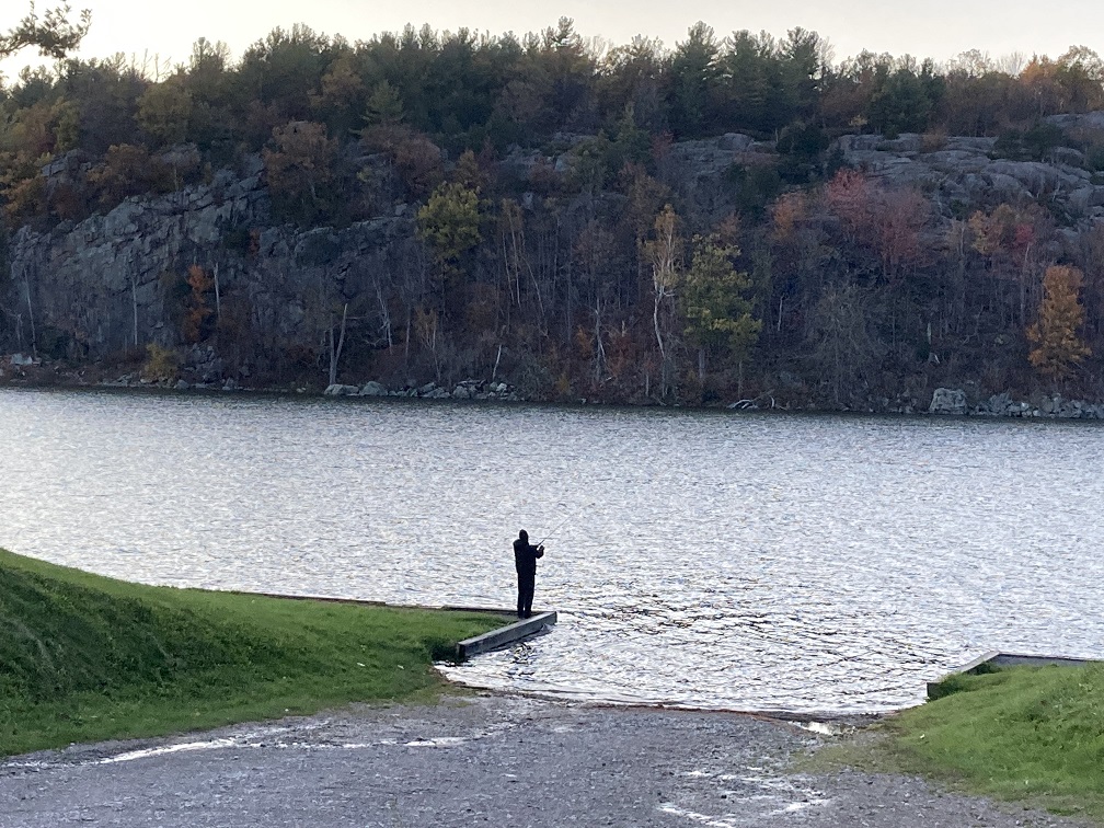 A man fishing from the boat launch area at Payne Lake with Pulpit Rock State Forest in the Background