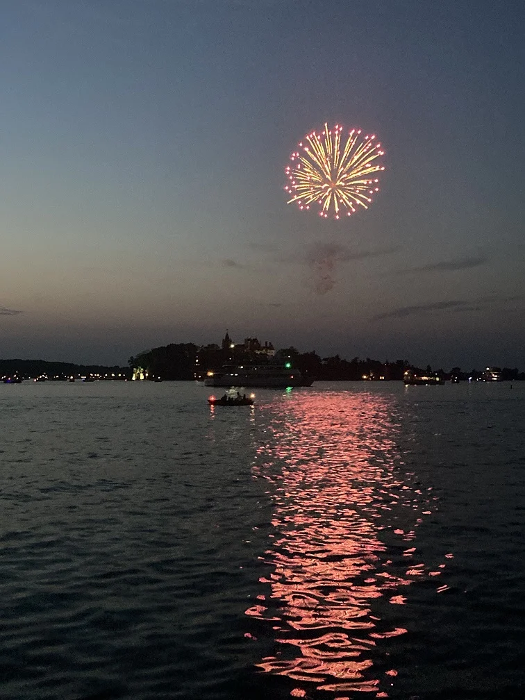 A nighttime photograph of a fireworks display over the St Lawrence River.  The photograph was taken from Alexandria Bay and Boldt Castle is in the background